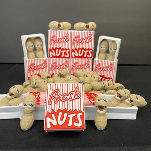 Puede incluir: Una exhibición de personajes de cacahuetes de dibujos animados y cajas de cacahuetes. Las cajas tienen rayas rojas y blancas y las palabras "Fresh NUTS". Los cacahuetes tienen caras sonrientes y están en varias poses.
