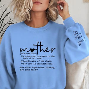 May include: Light blue sweatshirt with the word "mother" in black script, featuring a heart-shaped design over the "o". The definition of "mother" is printed below. The sleeve has the names "Ellie" and "Miall" written on it.