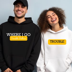 May include: Two black hooded sweatshirts with white text. One says "Where I Go Trouble Follows" with a yellow rectangle around the text "Trouble Follows". The other sweatshirt says "Trouble" in a yellow rectangle.