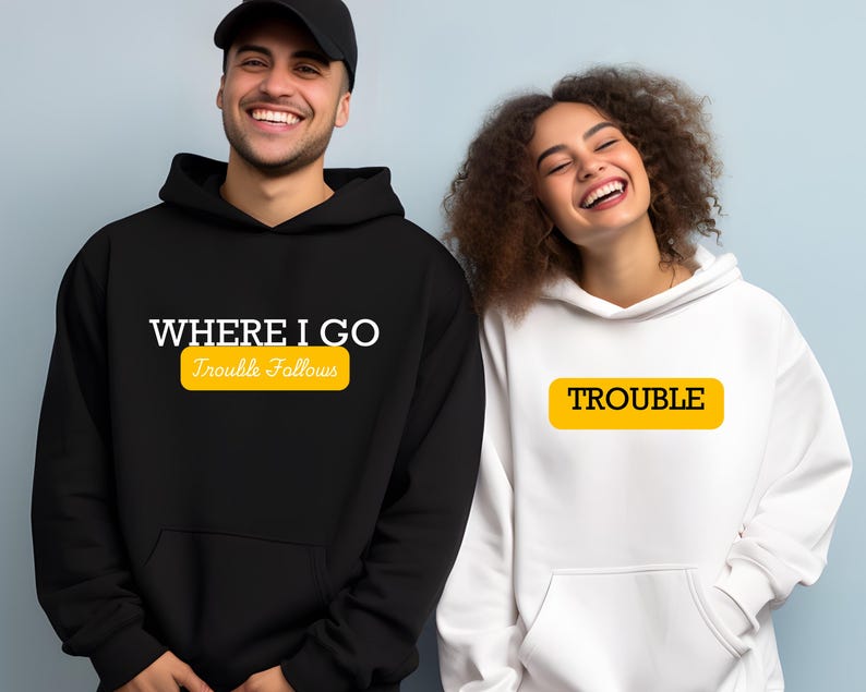 May include: Two black hooded sweatshirts with white text. One says "Where I Go Trouble Follows" with a yellow rectangle around the text "Trouble Follows". The other sweatshirt says "Trouble" in a yellow rectangle.