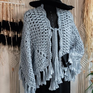 Könnte beinhalten: Ein hellblauer Häkel-Schal mit Fransenbesatz. Der Schal ist über eine schwarze Kleiderpuppe gelegt und ein schwarzer Hut liegt auf der Puppe.