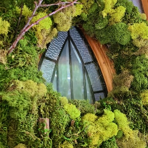 May include: A green moss wreath with a brown twig and a stained glass window in the background.