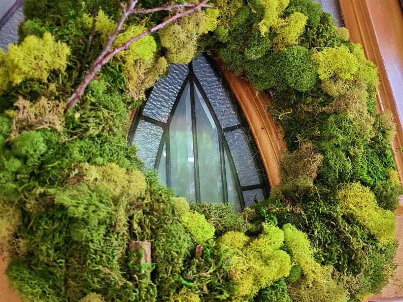 May include: A green moss wreath with a brown twig and a stained glass window in the background.