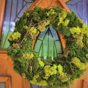 May include: A green moss wreath with brown twigs, hanging on a wooden door with a stained glass window.