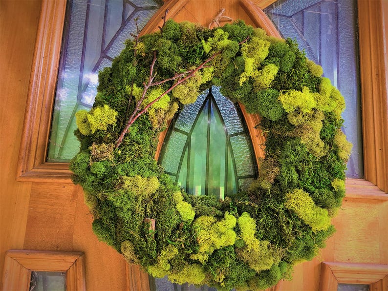 May include: A green moss wreath with brown twigs, hanging on a wooden door with a stained glass window.