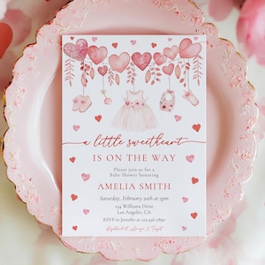 May include: A pink baby shower invitation with a watercolor design of hearts, flowers, and a baby dress. The text reads "a little sweetheart is on the way" and includes the name Amelia Smith, the date, and RSVP information.