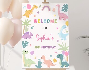 May include: Welcome to Sophia's 2nd Birthday sign with a rainbow, dinosaurs, and palm trees. The sign is white with colorful illustrations.