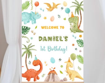 Op de afbeelding: Welkom op Daniel's 1e verjaardag! Een wit bord met een welkomstbericht en een dinosaurus thema. Het bord toont een groene, gele en oranje dinosaurus met een feestmuts, een blauwe dinosaurus met een feestmuts en een rode dinosaurus met een feestmuts. Het bord toont ook palmbomen, groene bladeren en kleurrijke bloemen.