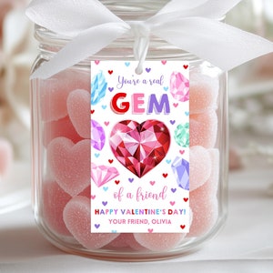 Puede incluir: Una etiqueta de regalo para el Día de San Valentín con una gema roja en forma de corazón y joyas de colores. La etiqueta dice "You're a real GEM of a friend HAPPY VALENTINE'S DAY! YOUR FRIEND, OLIVIA".