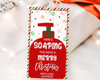 Op de afbeelding: Een rood en groen kerstcadeau-etiket met een cartoon-zeepfles en de tekst "Here's Soaping You Have A Merry Christmas With Love, Jackson".