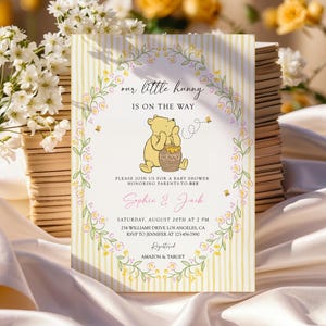 Może przedstawiać: Zaproszenie na baby shower z Kubusiem Puchatkiem. Zaproszenie ma żółte paski w tle i wieniec kwiatowy. Tekst zawiera "our little hunny is on the way" oraz szczegóły wydarzenia dla Sophie & Jack.