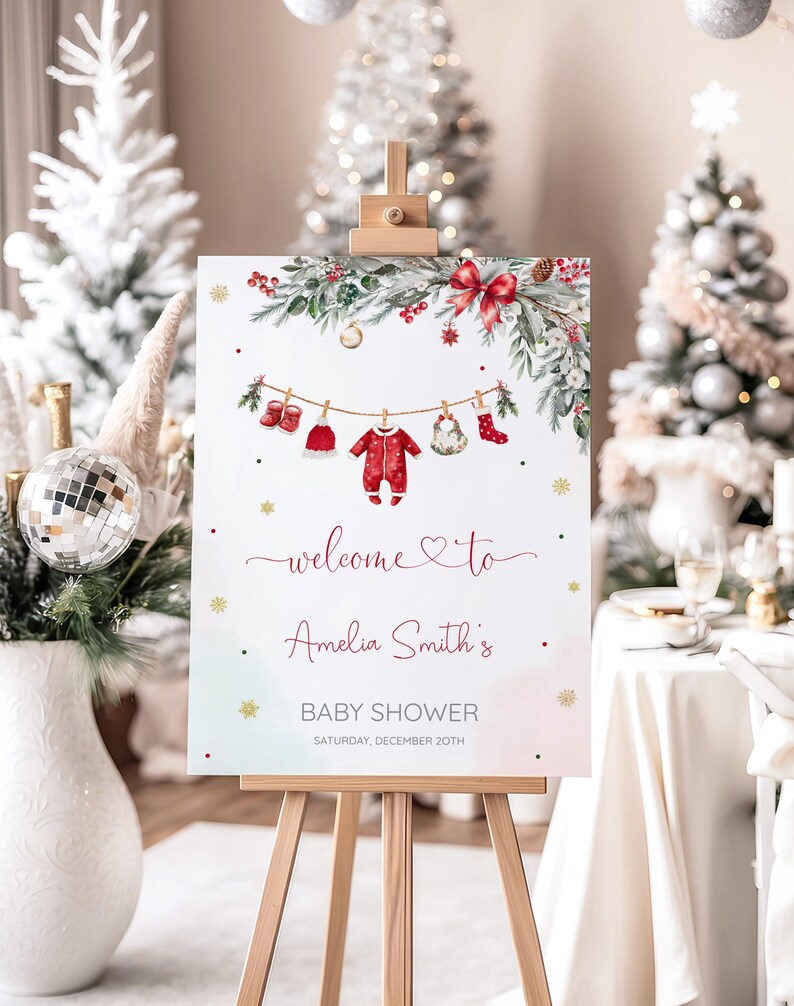 May include: A Christmas-themed baby shower sign on an easel. The sign displays a watercolour design with greenery, red accents, and baby clothes hanging on a line. Text reads "welcome to Amelia Smith's BABY SHOWER SATURDAY, DECEMBER 20TH."
