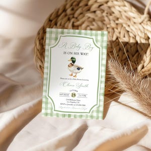 May include: A baby shower invitation with a green gingham border. The invitation features a watercolor illustration of a duck and the text "A Baby Boy Is On His Way!" with event details.