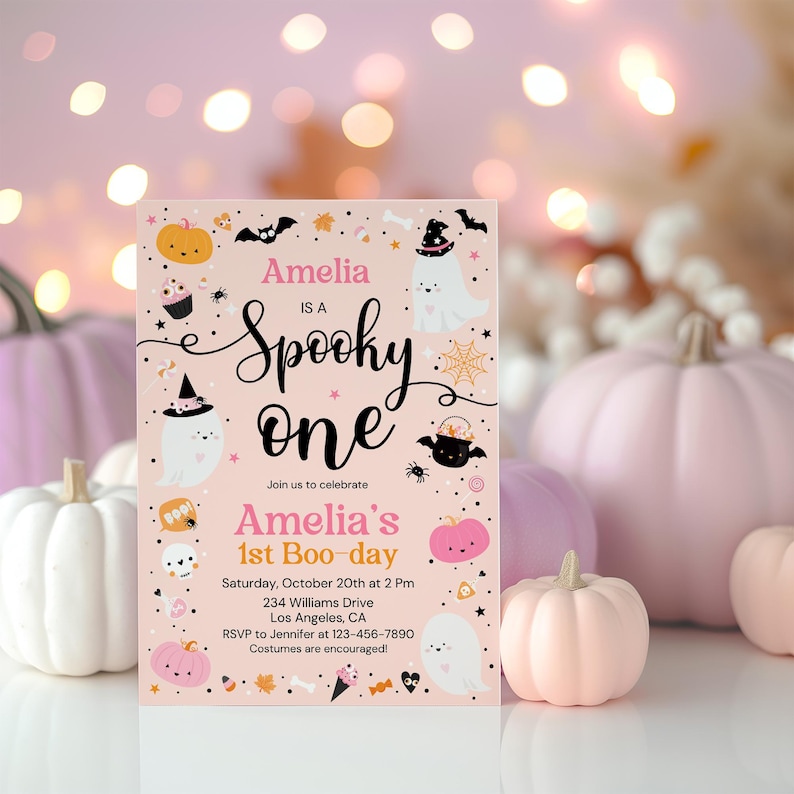 以下が含まれることがあります： 「Amelia is a Spooky One」と「Amelia's 1st Boo-day」のテキストが入った、ピンク色のハロウィーンをテーマにした招待状。カボチャ、幽霊、コウモリ、その他のハロウィーンの要素のイラストが特徴です。背景にはピンク色のカボチャがあります。
