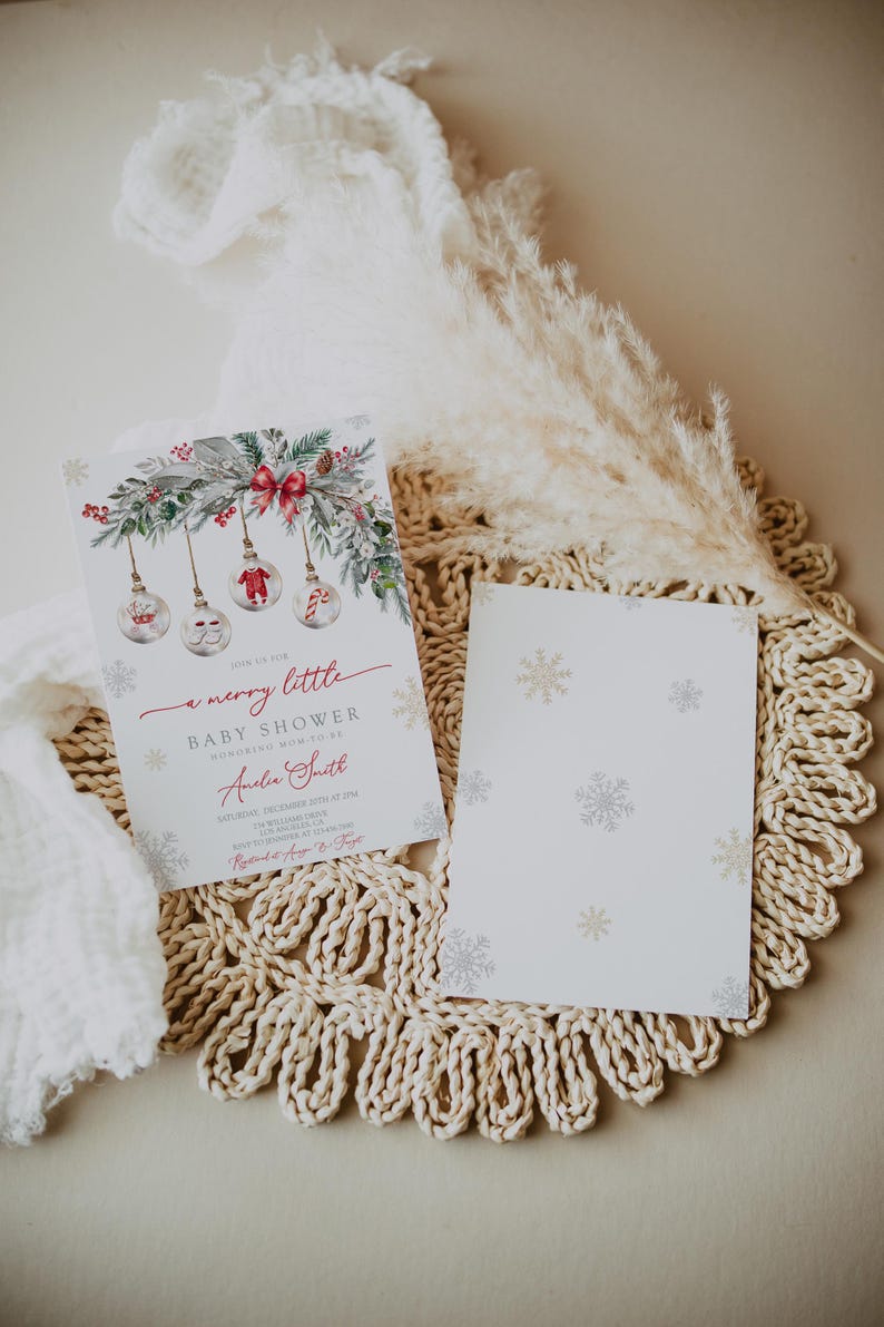 May include: A Christmas-themed baby shower invitation. The design includes watercolour ornaments, foliage, and a red bow. The text reads "a merry little baby shower". A blank card with snowflake patterns is also visible, all on a neutral background.