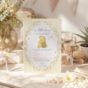 May include: A baby shower invitation with a Winnie the Pooh theme. The card features a yellow and white striped background, floral accents, and the text "our little hunny is on the way." The invitation includes the names Sophie & Jack.