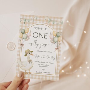 May include: A light brown and white checkered invitation with a cute cartoon goose wearing a hat and holding balloons. The text reads "Sophie is One silly goose" and includes details for a first birthday party.