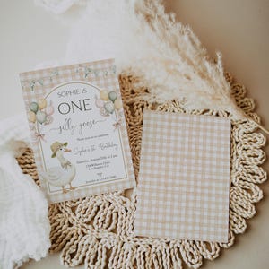 May include: A light brown and white gingham patterned invitation with a white goose illustration and the text "Sophie is One silly goose" and "Sophie's 1st Birthday".