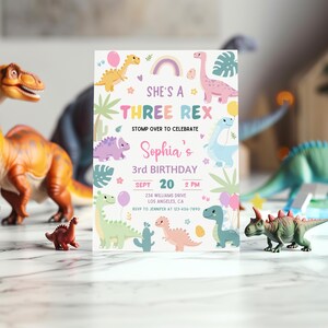 May include: A colourful invitation for a 3rd birthday party with a dinosaur theme. The invitation features a rainbow, a pink dinosaur, and the text "She's a Three Rex".