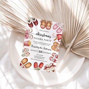 May include: A Christmas pyjama party invitation with a white background and colourful illustrations of slippers, popcorn, hot chocolate, and a snowman. The text reads "Please join us for a Christmas Pyjama Party. Put on your favourite jammies and join us for a festive fun! Hosted by the Andersons. Saturday | 23 | December. At 2:00 PM. 64 Williams Drive. Los Angeles, CA."