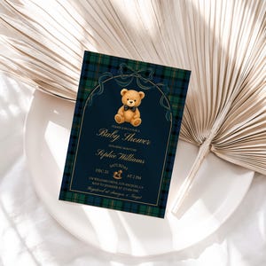 May include: A baby shower invitation with a navy blue background and a plaid border. The invitation features a teddy bear illustration and gold text that reads "Baby Shower" and the name "Sophie Williams".