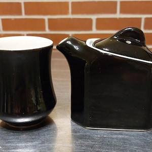 May include: A black ceramic tea set with a teapot and a mug. The teapot has a lid and a handle. The mug has a handle.