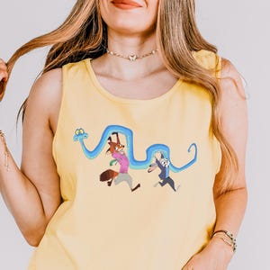 A woman wearing a yellow tank top with a cartoon character design and holding her hair.