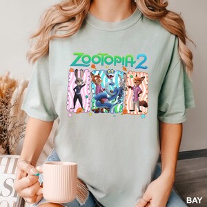 A person wearing a t-shirt with a graphic of the characters from the animated film "Zootopia 2" and holding a coffee mug.