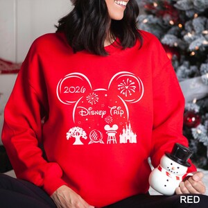 A woman wearing a red sweater with a white design on it, holding a snowman and a mug.