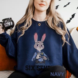 A woman wearing a navy blue sweatshirt with a cartoon image of a police officer and the text "Six Seven Navy" printed on it.
