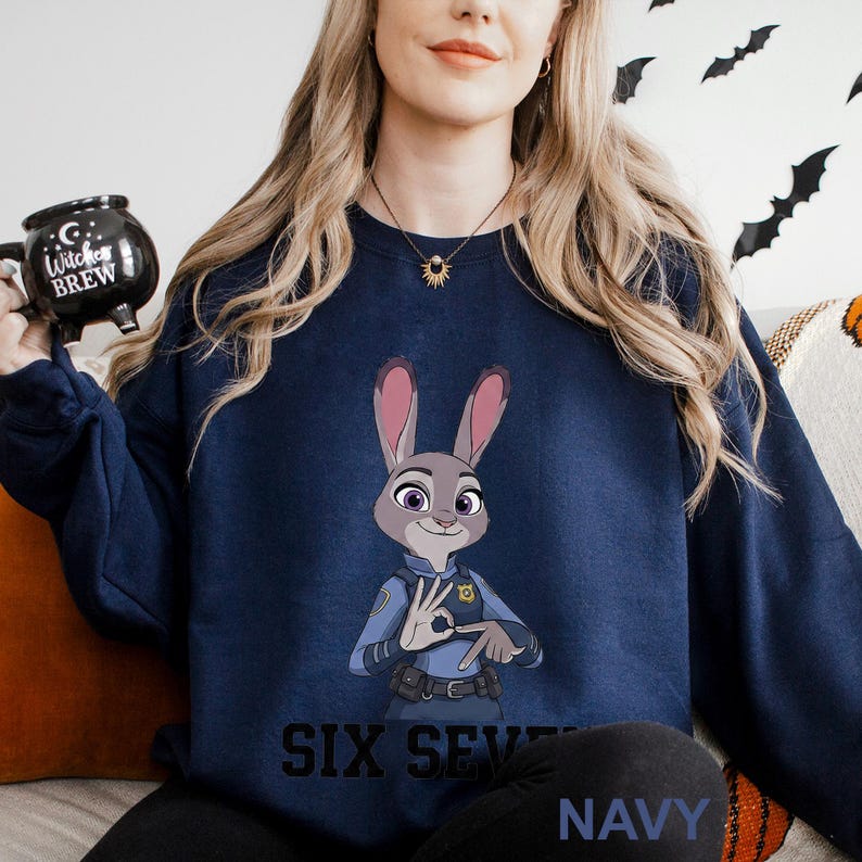 A woman wearing a navy blue sweatshirt with a cartoon image of a police officer and the text "Six Seven Navy" printed on it.