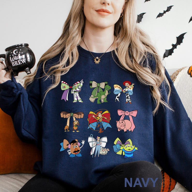 A woman wearing a navy blue sweatshirt with various cartoon characters printed on it, including characters from the Toy Story franchise. She is holding a black mug with the words "Toy Story Brew" printed on it.