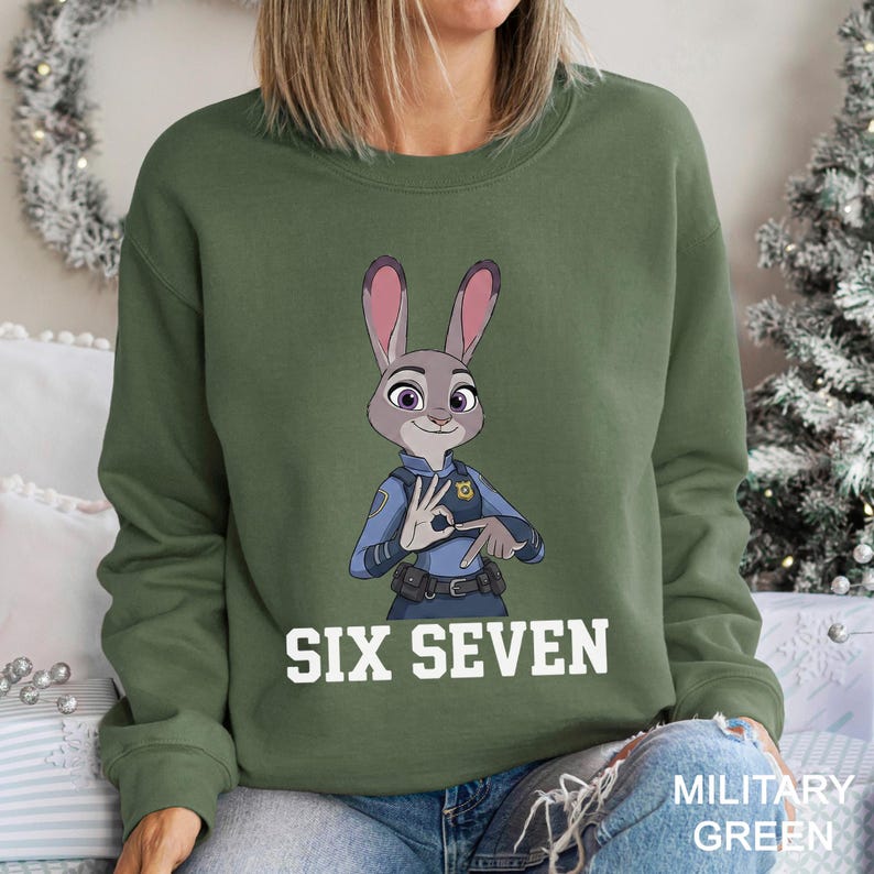 A woman wearing a green sweatshirt with a cartoon image of a police officer and the text "SIX SEVEN" printed on it.