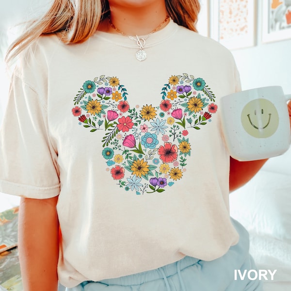 Könnte beinhalten: Ein weißes T-Shirt mit einem floralen Mickey Mouse-Design. Das Design ist in den Farben Rosa, Gelb, Blau und Grün gehalten. Das Shirt ist mit "IVORY" gekennzeichnet.