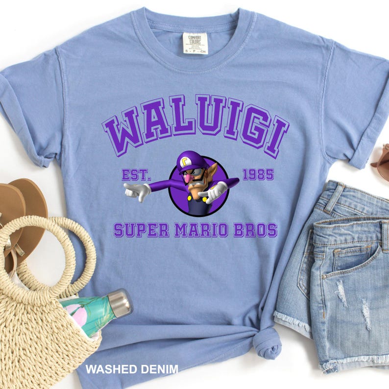 A blue t-shirt with a purple graphic and text, a pair of denim shorts, a straw hat, and a bottle of sunscreen.