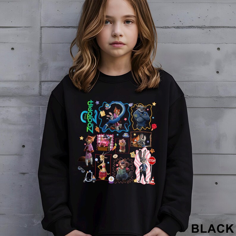 A young girl wearing a black sweatshirt with a colorful collage of cartoon characters and illustrations on it.