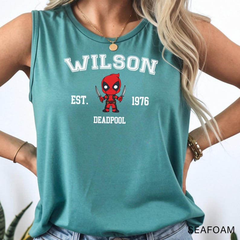 A woman wearing a green tank top with a graphic of a character from the Marvel Cinematic Universe, specifically Deadpool.