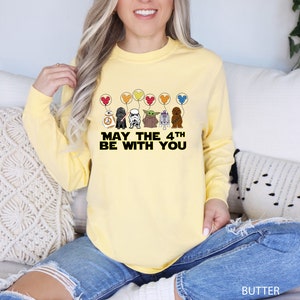 a woman sitting on a couch wearing a yellow shirt that says may the 4th be
