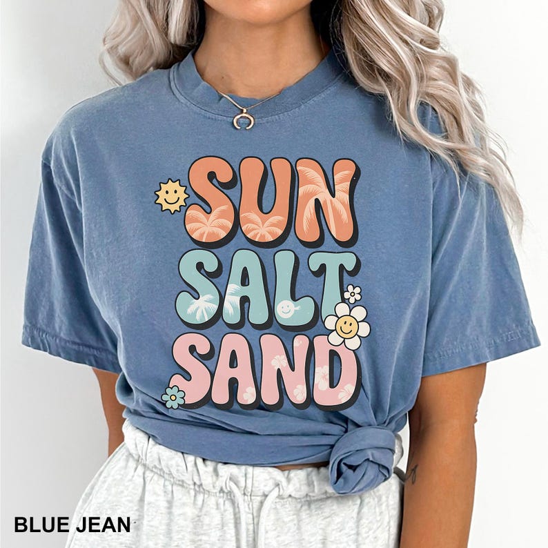 A woman wearing a blue t-shirt with the text "SUN SALT SAND" printed on it.