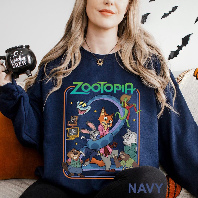 A woman wearing a navy blue sweatshirt with a cartoon character design, including a fox, rabbit, and other animals, is holding a black mug with the text "Zootopia" on it.