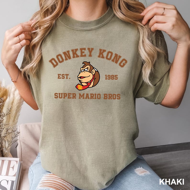 A person wearing a green t-shirt with a graphic of a Donkey Kong character and text that says "Donkey Kong EST. 1985 SUPER MARIO BROS".