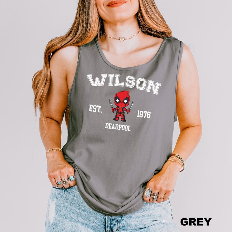 A woman wearing a grey tank top with a graphic of a character from the Marvel Cinematic Universe, specifically Deadpool.