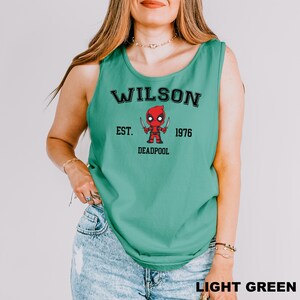 A woman wearing a green tank top with a graphic of a character from the Marvel Cinematic Universe, specifically Deadpool.