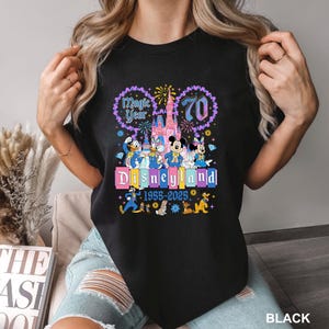 A woman wearing a black t-shirt with a colorful graphic design celebrating the 70th anniversary of Disneyland.