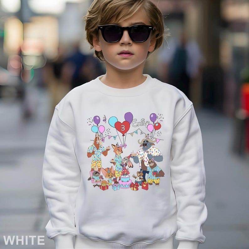 A young boy wearing a white sweatshirt with a colorful cartoon character design and a birthday theme.
