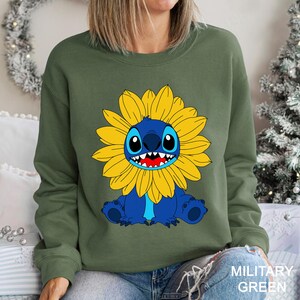 A woman wearing a green sweatshirt with a cartoon character of a blue cat with a yellow flower on its chest.