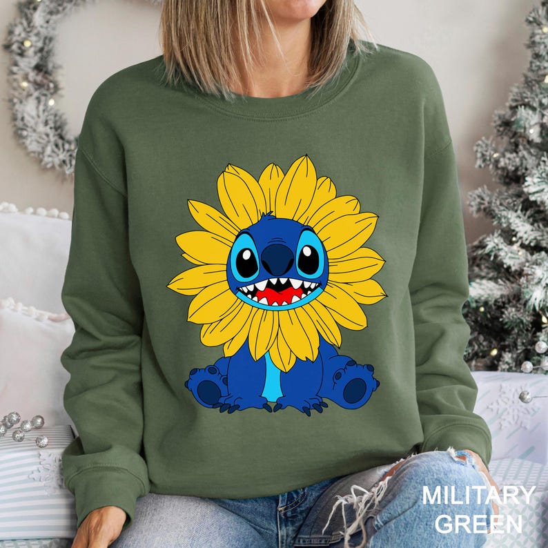 A woman wearing a green sweatshirt with a cartoon character of a blue cat with a yellow flower on its chest.
