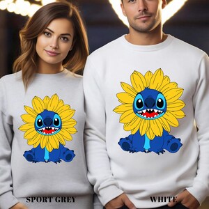 A woman and a man are standing next to each other, both wearing white sweatshirts with a cartoon character printed on them.