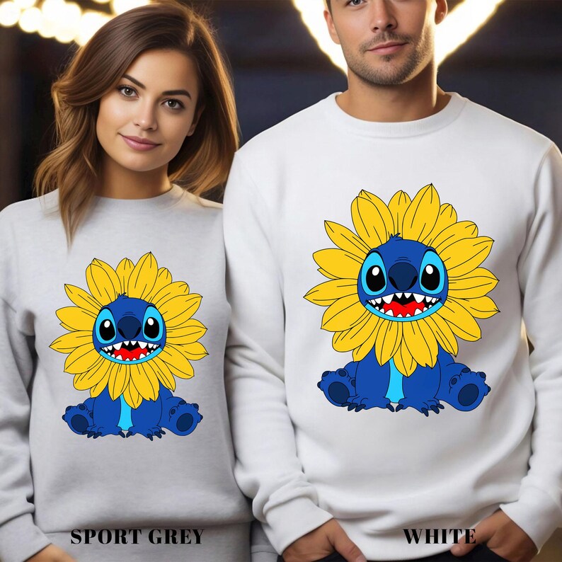 A woman and a man are standing next to each other, both wearing white sweatshirts with a cartoon character printed on them.