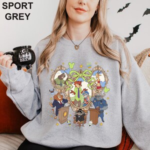A woman wearing a grey sweatshirt with a cartoon character design, holding a black mug with the text "I love Brew" printed on it.